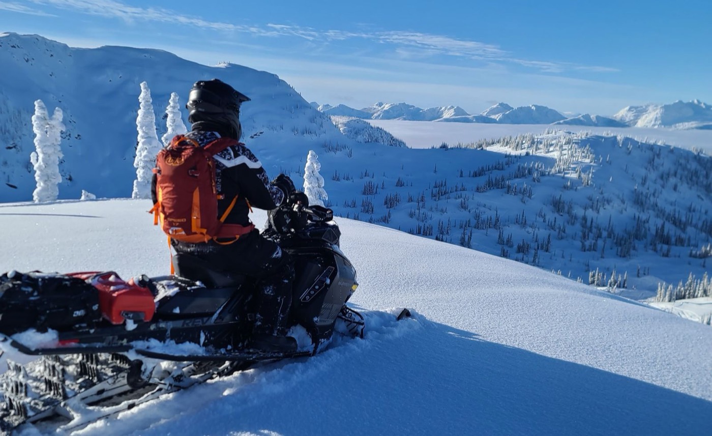 Snowmobiler on a ridge above a cloud-filled valley in the BC backcountry