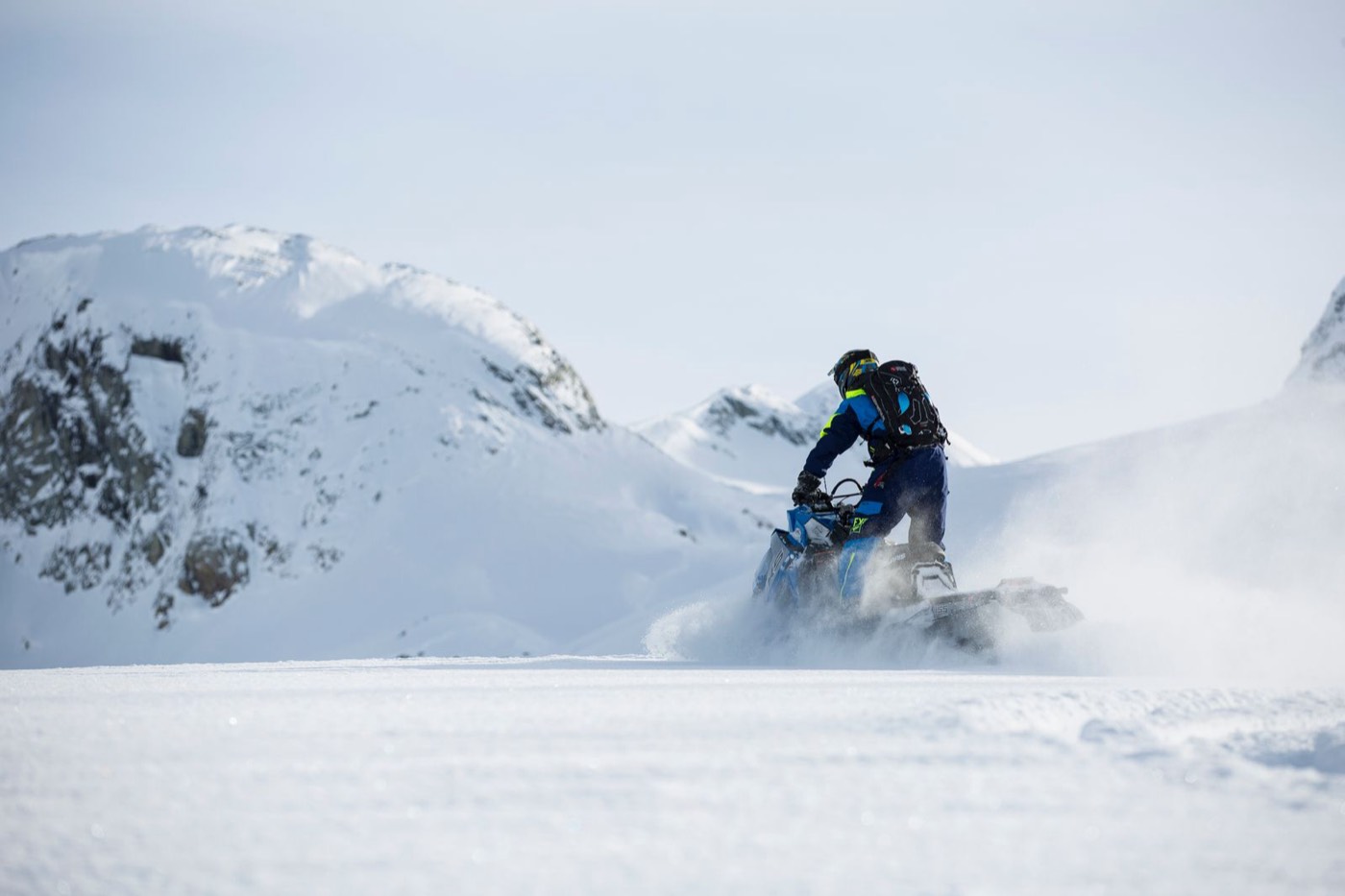 Snowmobiler powering through powder toward alpine peaks