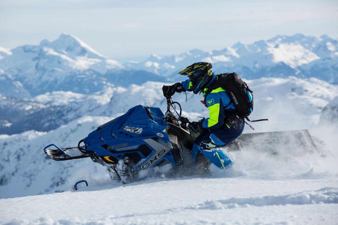 Rider side-hilling a mountain sled with peaks behind